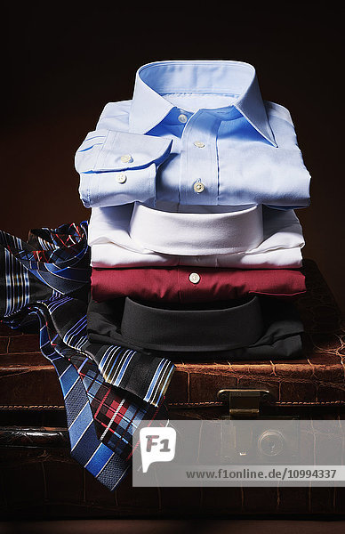 Stapel von Hemden mit Krawatten auf einem Koffer im Atelier
