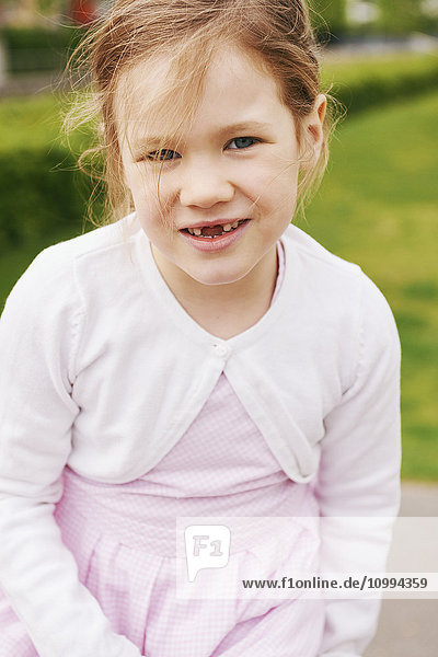 Porträt eines 5-jährigen Mädchens in rosa Kleid und weißem Pullover  das lächelnd in die Kamera schaut und zeigt  dass ihm die Vorderzähne fehlen