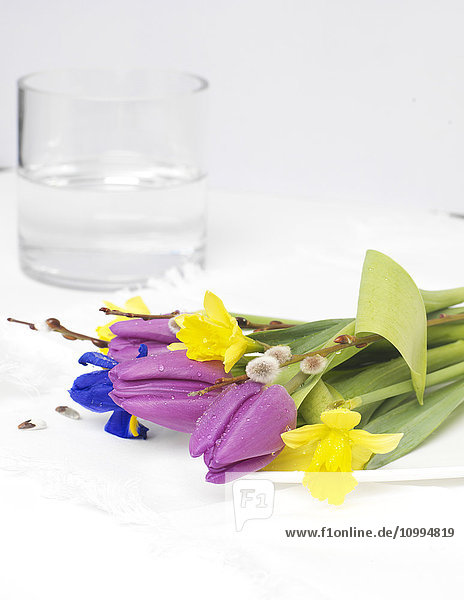 Nahaufnahme eines Frühlingsblumenstraußes auf einem Teller mit einer Vase mit Wasser