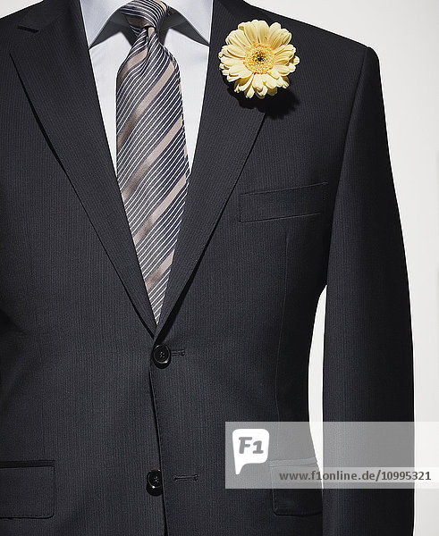 Detail einer dunkelblauen Anzugsjacke mit grauem Hemd und gestreifter Krawatte und gelber Blume