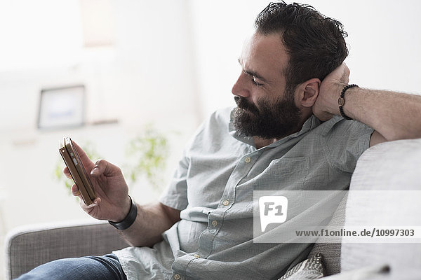 Mid-adult man using smartphone on couch