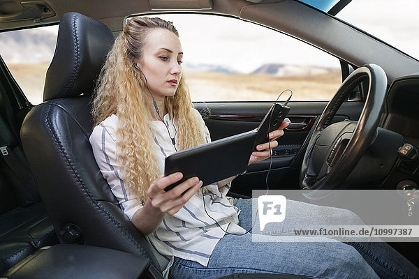 Frau sitzt im Auto und benutzt gleichzeitig Tablet und Mobiltelefon