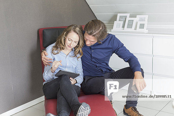 Mid-adult couple sitting on armchair and using tablet