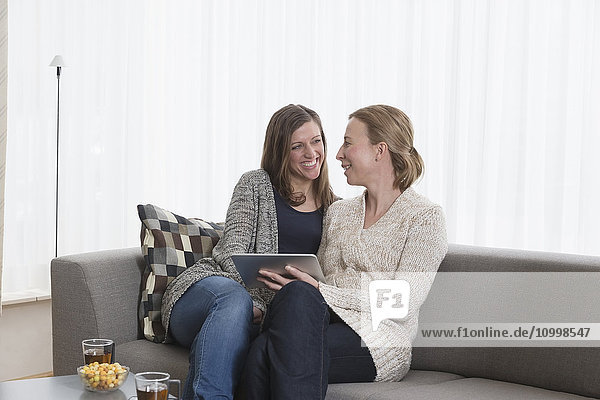 Lächelnde Frauen sitzen auf dem Sofa im Wohnzimmer und halten ein Tablet