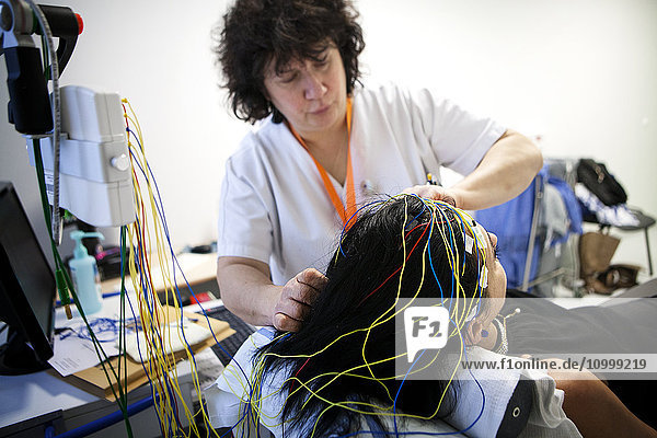 Reportage in a functional neurological exploration unit. Epilepsy screening and follow-up consultation. The patients take a video EEG (electroencephalogram)  during which they are subjected to various stimuli  both auditive and visual. The patterns are then analysed by the neurologist. A nurse sets up electrodes.