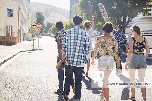 Teenage friends with skateboards walking on sunny urban street