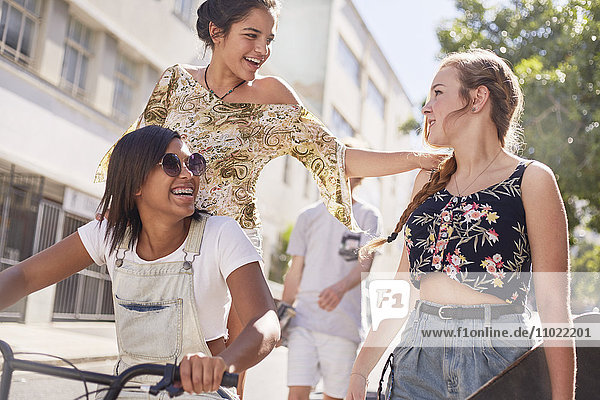Teenager-Mädchen mit BMX-Fahrrad und Skateboard auf der sonnigen Stadtstraße