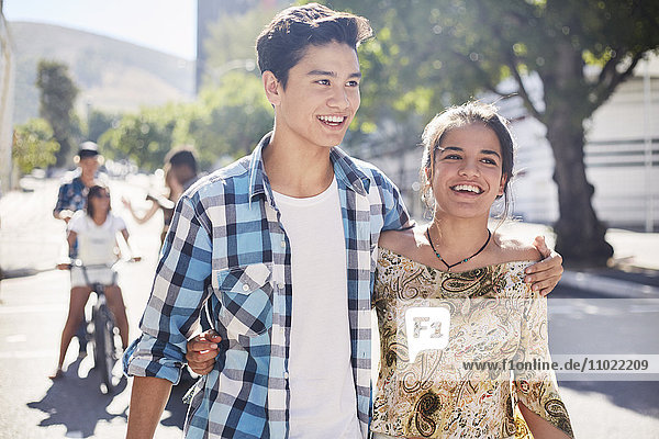 Lächelndes Teenager-Paar  das auf einer sonnigen  städtischen Straße spazieren geht.