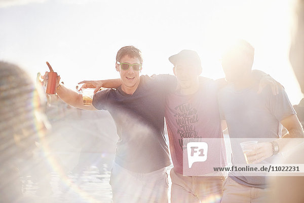 Portrait junge Männer beim Biertrinken auf der sonnigen Poolparty