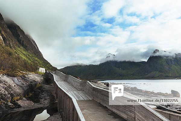 Boardwalk leading towards mountains against cloudy sky