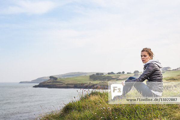 Side view portrait of woman sitting on hill by sea against sky