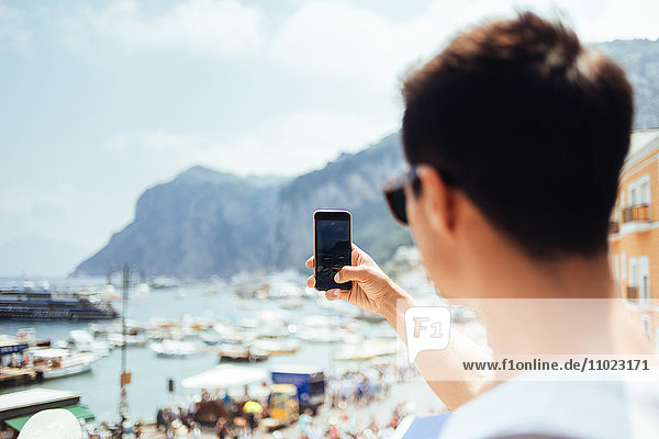 Young man photographing through smart phone at Marina Grande against sky