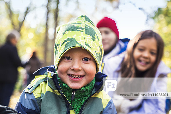 Portrait of happy boy wearing warm clothing with family in background at forest