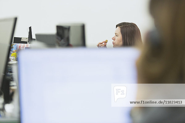 Geschäftsfrau beim Essen und Arbeiten am Schreibtisch im Büro