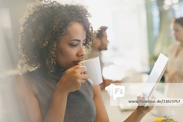 Geschäftsfrau trinkt Kaffee und benutzt ein digitales Tablet