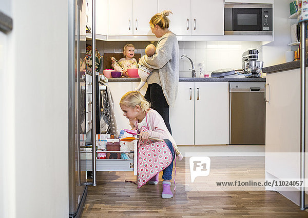 Girl searching in drawer while mother carrying baby in kitchen