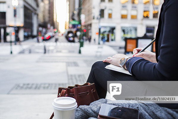 Cropped image of woman writing by city street