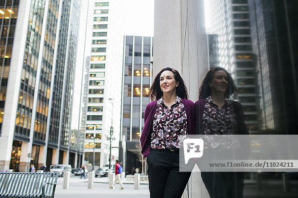 Low angle view of smiling businesswoman standing by glass window in city