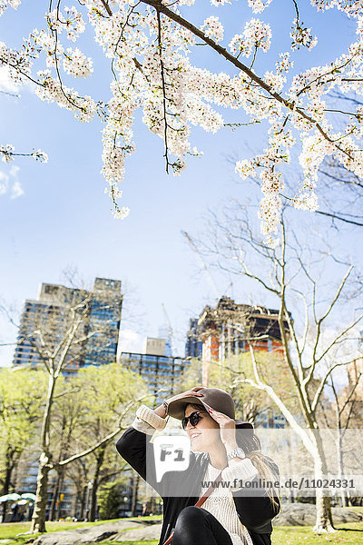 Junge Frau hält Hut und sitzt an einem Gebäude im Central Park