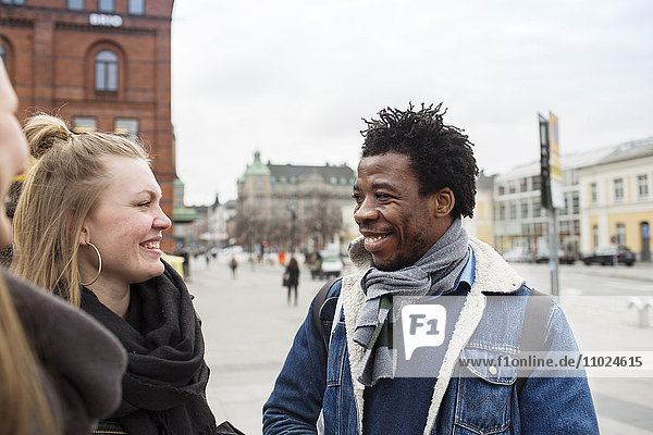 Smiling friends talking while standing in city against clear sky