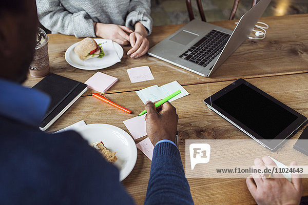 Cropped image of friends working while having sandwich at cafe