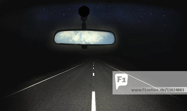 Blauer Himmel im Rückspiegel eines Autos mit dunkler Straße geradeaus