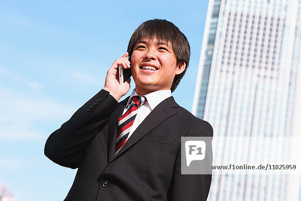 Junger japanischer Geschäftsmann am Telefon