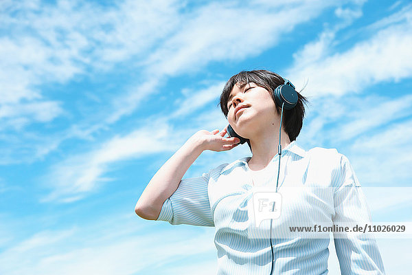 Junge japanische Frau entspannt sich unter dem blauen Himmel