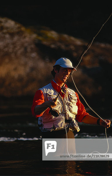 Ein Mann in Fischerkleidung steht im Wasser und fischt.