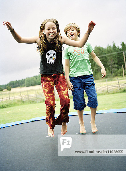 A girl and a boy jumping on a trampoline.