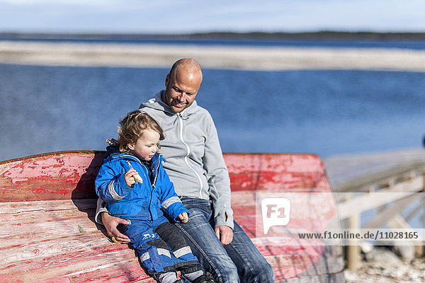 Vater und Sohn sitzen auf einem Boot am Strand