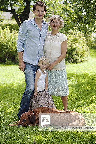 Porträt der Eltern mit Tochter und Hund im Garten
