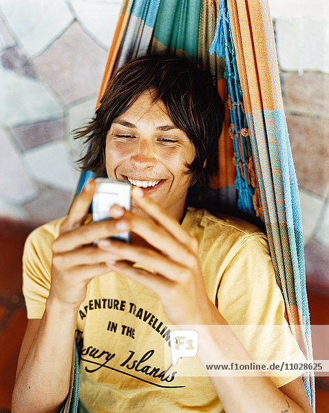 Ein junger Mann mit einem Mobiltelefon in einer Hängematte.