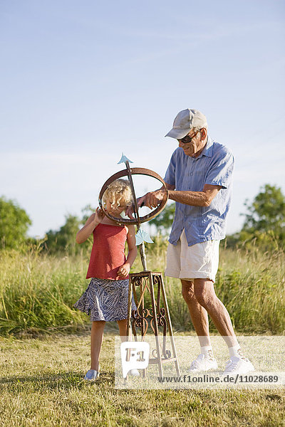 Grandfather showing granddaughter sundial in field
