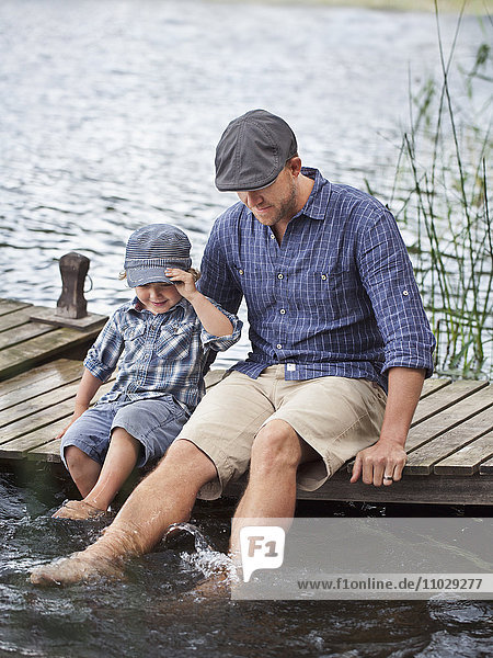 Mann mit Sohn sitzt auf dem Steg am See