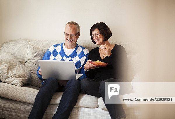 Älteres Paar sitzt auf dem Sofa und schaut auf den Laptop