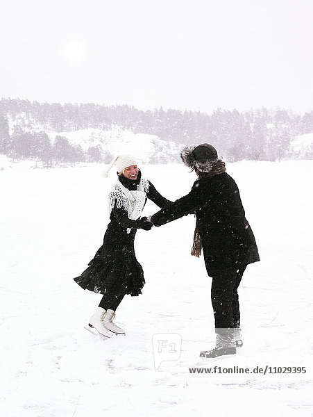 Ein Mann und eine Frau laufen Schlittschuh und halten sich an den Händen.