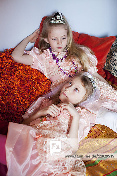 Zwei Mädchen in eleganten Kleidern und Halsketten entspannen sich auf dem Bett
