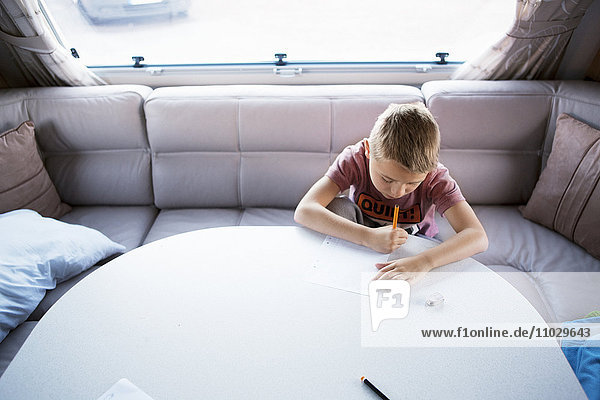 Junge im Wohnmobil schreibt am Tisch