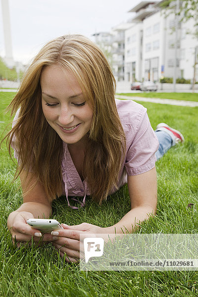 Porträt einer Frau  die im Gras liegt und ein Mobiltelefon benutzt