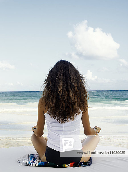 Junge Frau meditiert am Strand  Rückansicht