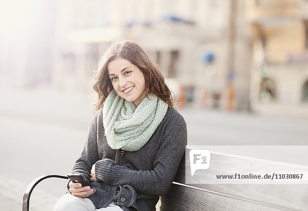 Porträt einer jungen Frau  die auf einer Bank sitzt und telefoniert