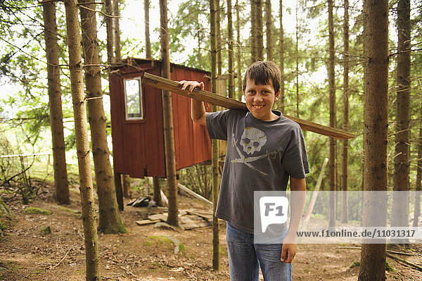 Jugendlicher  der eine Holzplanke vor einer Hütte trägt