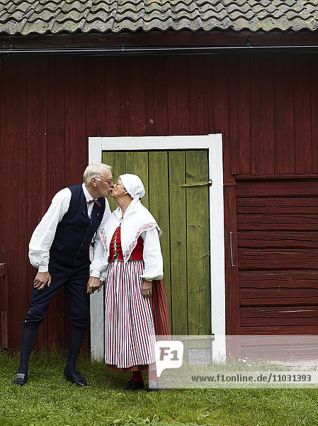 Älteres Paar in Tracht küsst sich vor einem Haus  Dalarna  Schweden