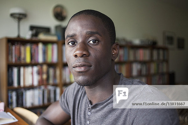 Porträt eines jungen schwarzen Mannes mit Bücherregalen im Hintergrund