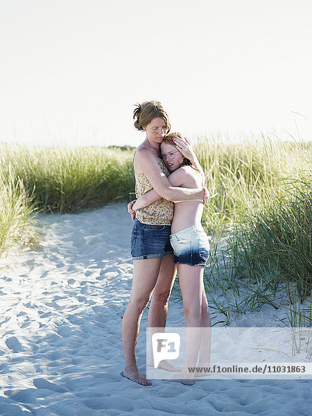 Mutter umarmt jugendliche Tochter am Strand