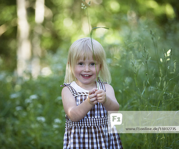Portrait of smiling girl holding grass on meadow