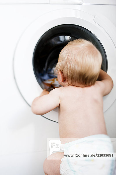 Baby boy wearing diaper looking into washing machine
