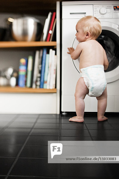 Baby boy wearing diaper standing in kitchen