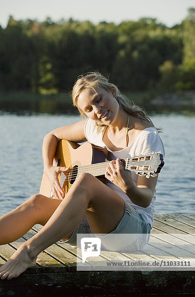 Junge Frau auf dem Bootssteg spielt Gitarre